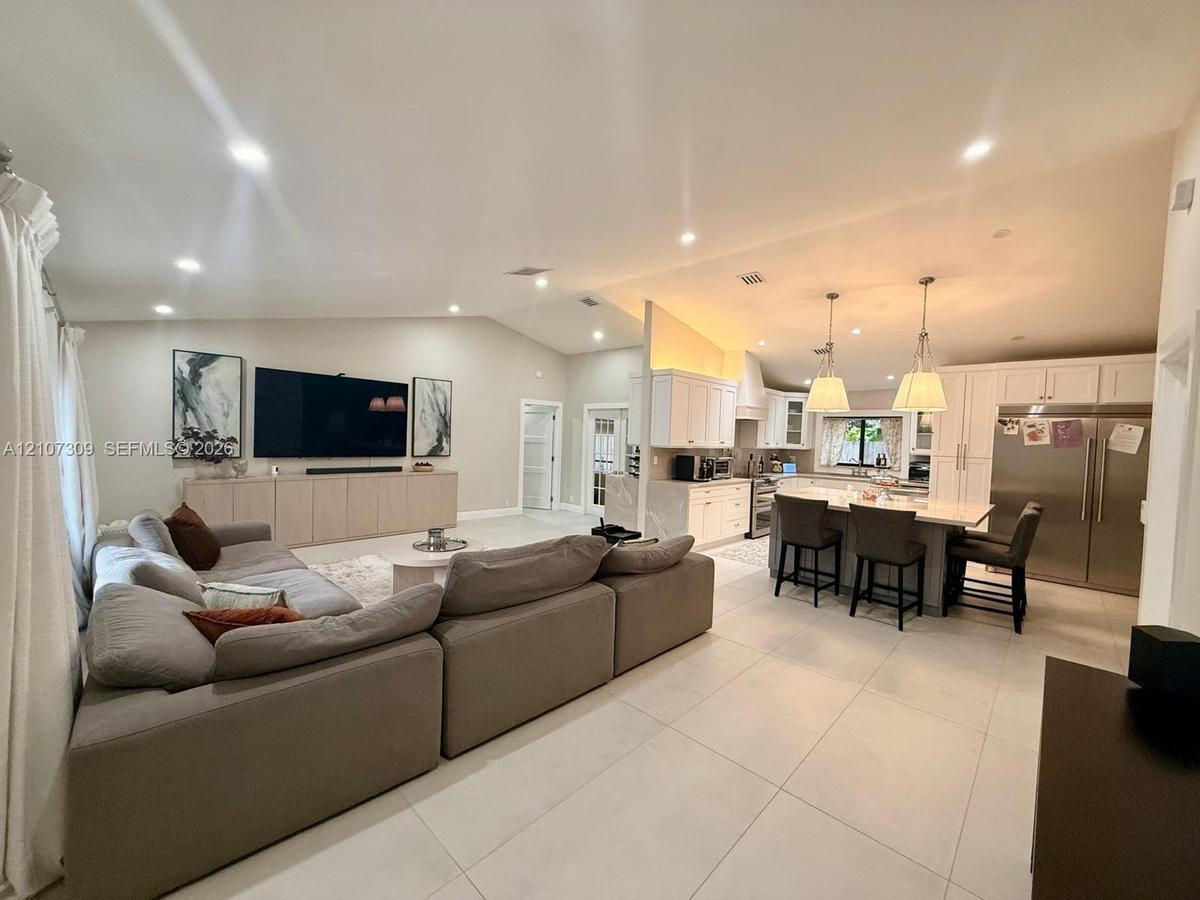 Open-concept interior featuring vaulted ceilings, light-toned large-format tile flooring, a kitchen island with stone countertops, and recessed lighti
