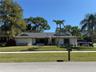 Single-story exterior featuring a light-toned stucco façade, a shingled roof, contrasting window shutters, and established palm trees