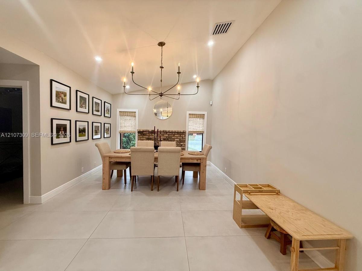 Large-format tile flooring, vaulted ceilings, multi-arm metal chandelier, and a decorative brick fireplace surround