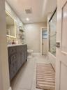 Bathroom featuring a grey shaker-style vanity with stone-surface countertop, LED-backlit mirror, large-format floor tile, and a shower-tub combination