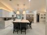 Kitchen featuring white cabinetry, a central island with a stone countertop, stainless steel refrigerator, stone-style flooring, and dual pendant ligh