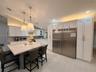 Kitchen featuring white shaker-style cabinetry, a large central island with light-toned stone countertop, stainless steel refrigerator with custom pan
