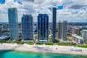High-rise coastal development featuring glass-paneled architecture, direct oceanfront access, extensive white sand shoreline, and ground-level pool fa
