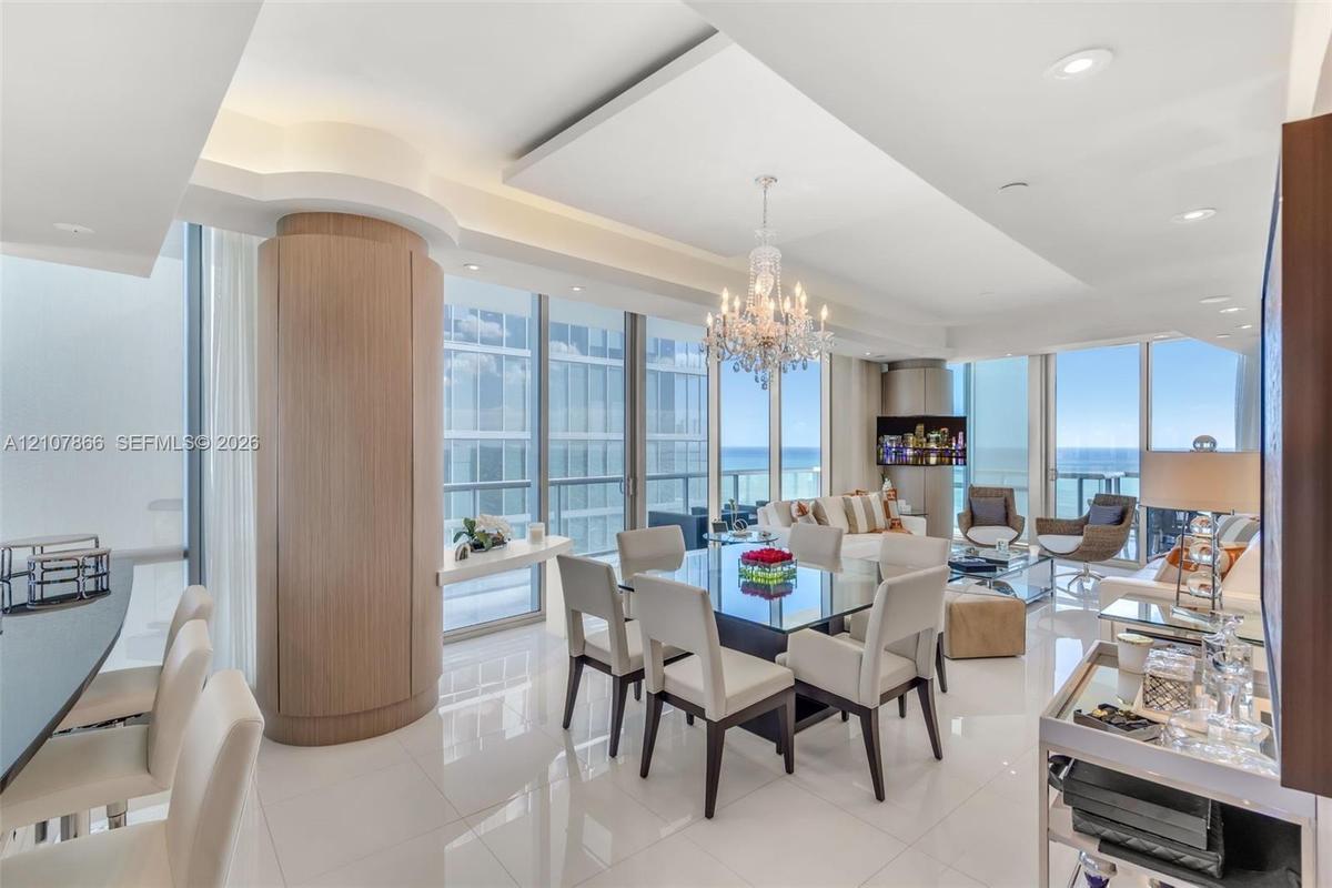 Open-concept interior featuring polished tile flooring, tray ceilings with recessed lighting, floor-to-ceiling glass windows, a circular wood-finish a
