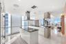 Contemporary kitchen featuring a center island with a sleek cooktop, stainless steel chimney-style range hood, high-gloss cabinetry, floor-to-ceiling 