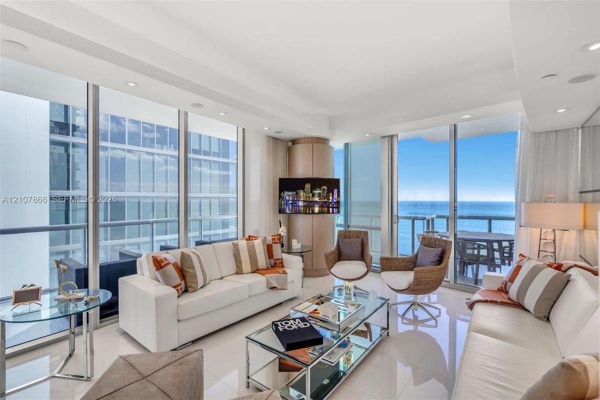 Floor-to-ceiling glass walls, polished tile flooring, recessed lighting, and a wrap-around balcony with ocean scenery