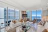 Floor-to-ceiling glass walls, polished tile flooring, recessed lighting, and a wrap-around balcony with ocean scenery