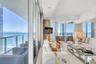 Floor-to-ceiling glass walls, expansive private balcony with metal railing, polished stone flooring, recessed ceiling lighting, and built-in rounded c