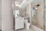 Bathroom featuring a white vanity with a vessel sink, a full-length wall mirror, a glass-enclosed walk-in shower with stone-tile surround, and a rain-