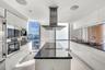 Modern kitchen featuring high-gloss white cabinetry, a center island with a dark solid-surface countertop, stainless steel integrated wall ovens, a ce