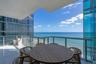 Covered balcony featuring glass paneled railings, white tile flooring, and ocean frontage