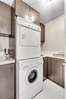 Laundry area featuring floor-to-ceiling dark-finish cabinetry, stacked washer and dryer unit, solid-surface countertops, and an integrated basin