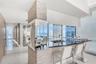 Stone-clad structural pillar, polished dark countertop, stainless steel dual-basin undermount sink, floor-to-ceiling glass windows, and glossy tile fl