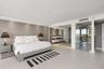 Neutral-toned interior space featuring large-format tile flooring, recessed ceiling lighting, textured accent wall, and glass-enclosed bathroom area