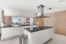 Modern kitchen featuring white flat-panel cabinetry, dark stone countertops, stainless steel island-mounted range hood, built-in cooktop, and wood-fin