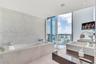 Drop-in bathtub with stone-finish surround, textured pebble-style accent wall, dual rectangular vessel sinks, polished stone countertop, and floor-to-