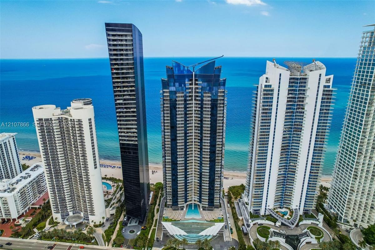 High-rise residential tower featuring a glass facade, private balconies, and an outdoor swimming pool situated along the beachfront