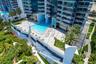 High-rise complex featuring an expansive elevated pool terrace, glass-railing balconies, stone-paver decking, and landscaped green spaces