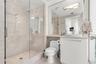 Glass-enclosed walk-in shower with tile surround, neutral-tone wall tile, white cabinetry, integrated sink, and large vanity mirror