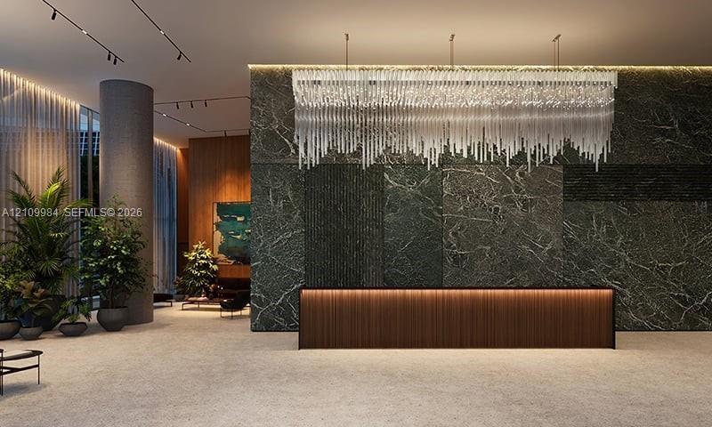 Lobby featuring a stone-clad accent wall, linear crystal chandelier, integrated under-cabinet lighting, wood-panel reception desk, and recessed track 