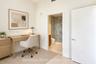 Neutral wall finishes with a full-height doorway opening to a bathroom featuring stone-patterned tile flooring, a glass-enclosed shower with large-for