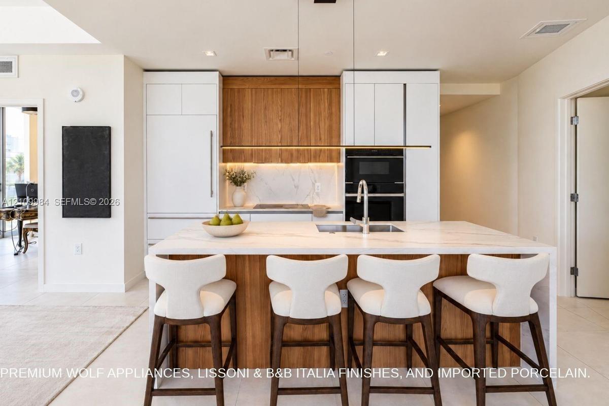 Kitchen featuring an expansive center island with a stone-finish countertop, integrated built-in appliances, flat-panel cabinetry in white and natural