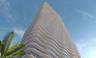 High-rise architectural exterior featuring a curvilinear facade, stacked undulating floor plates, and glass-encased balcony perimeters
