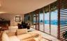 Floor-to-ceiling glass walls, integrated wooden privacy screens, recessed ceiling lighting, light-toned stone flooring, and a wide-span exterior deck