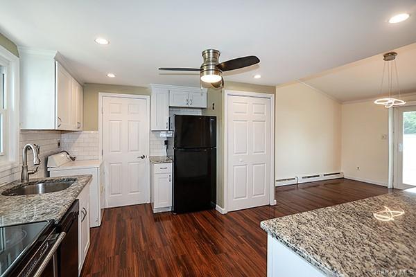 Kitchen with light stone countertops, white cabinets, tasteful backsplash, black appliances, and dark wood-style floors