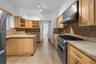 Kitchen featuring natural wood cabinetry, stone countertops, stone backsplash, stainless steel gas range with overhead vent hood, and wood-finish floo