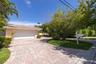 Attached two-car garage with a horizontal-panel door, expansive paver driveway, and mature landscaping