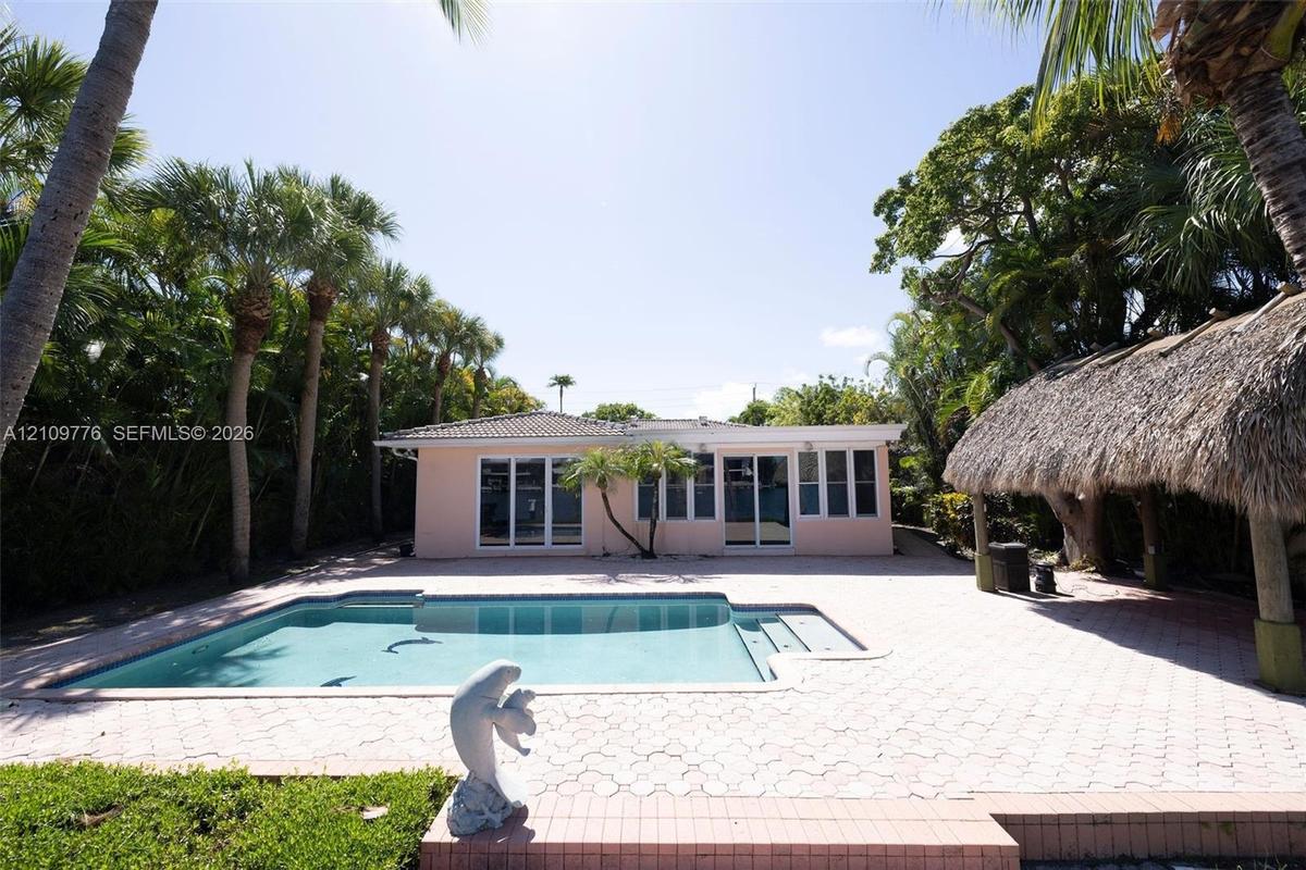 Outdoor area featuring a private in-ground swimming pool, expansive paver patio, thatched-roof tiki structure, and mature palm landscaping