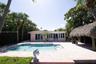 Outdoor area featuring a private in-ground swimming pool, expansive paver patio, thatched-roof tiki structure, and mature palm landscaping
