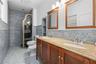 Dual-sink vanity with wood cabinetry, stone-finish countertop, decorative mosaic tile backsplash, built-in shelving, and framed wall mirrors