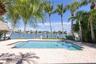 Waterfront swimming pool with paver decking, thatched-roof structure, and private boat dock