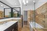 Bathroom featuring natural stone wall and floor tiling, dark-toned vanity with an integrated white countertop, frameless glass shower enclosure, and r