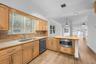Kitchen featuring light wood cabinetry, stone countertops, integrated stainless steel microwave, undermount sink, and wood-finish flooring