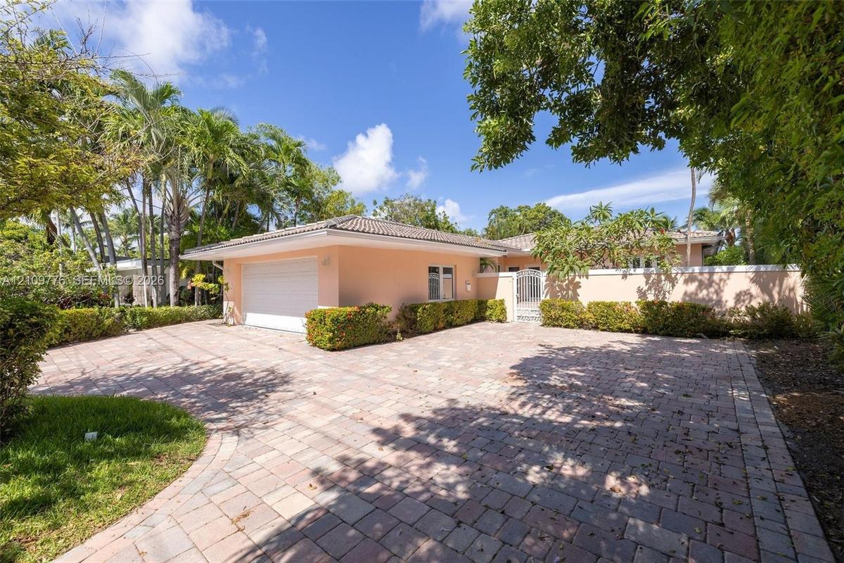 Paver driveway leading to a two-car garage with a tile roof, enclosed by a perimeter wall and mature tropical landscaping