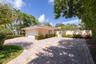 Paver driveway leading to a two-car garage with a tile roof, enclosed by a perimeter wall and mature tropical landscaping