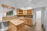 Kitchen featuring natural wood cabinetry, stone countertops, stone backsplash, wood-finish flooring, and a single-pane window with a wood trim accent