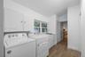 Laundry room featuring wood-finish flooring, white cabinetry, a utility sink, and white appliances