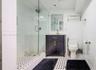 Bathroom featuring a walk-in shower with glass enclosure, dark wood-finish vanity with metallic hardware, wall-mounted mirror, and patterned mosaic ti