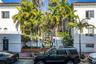 Stucco facade with articulated molding, decorative metal gate, and mature palm trees