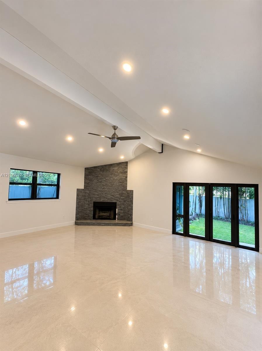 Vaulted ceiling with recessed lighting, stone-surround fireplace, polished tile flooring, ceiling fan, and black-framed multi-panel sliding glass door