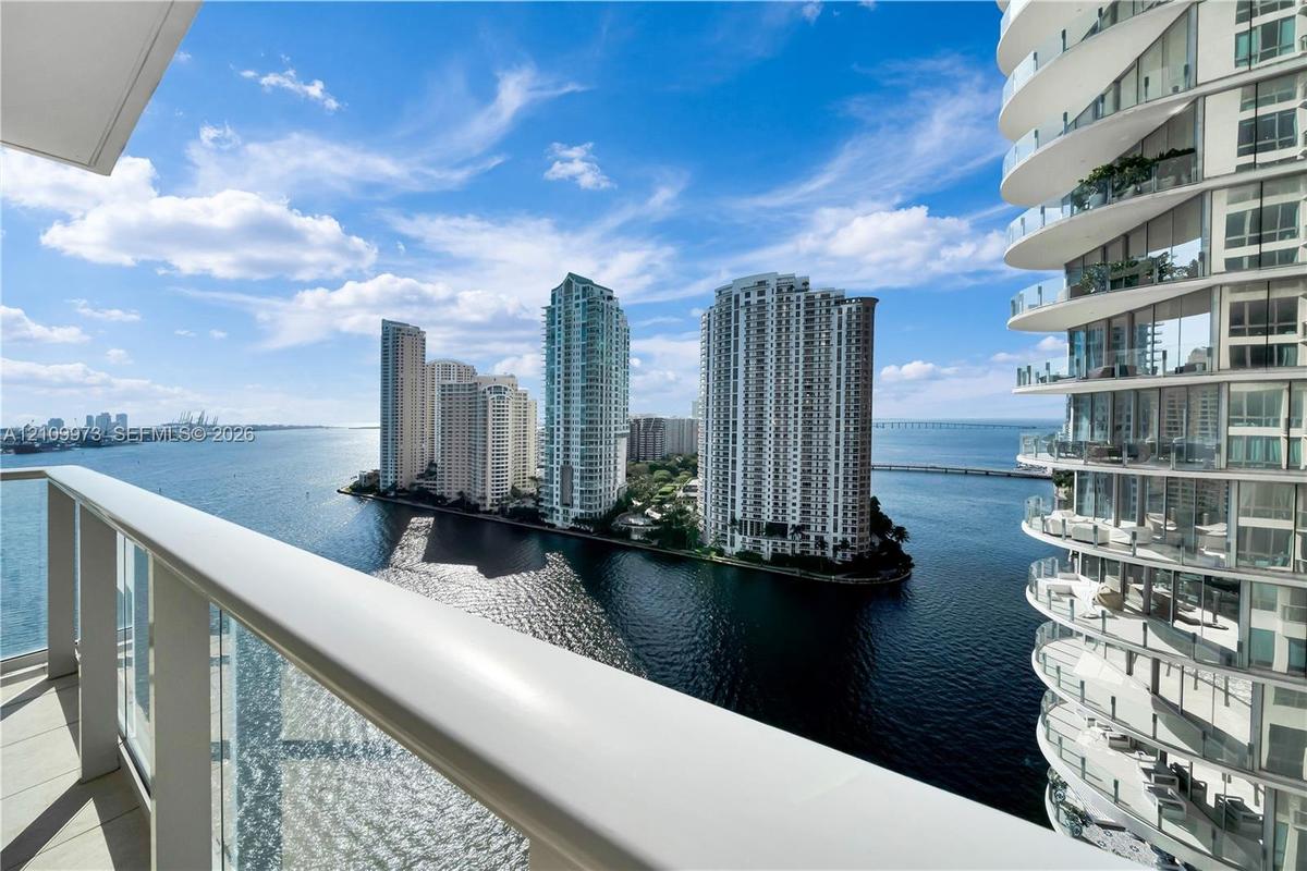 Covered balcony with glass-paneled railing overlooking the waterfront and cityscape