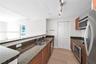 Kitchen featuring wood-finish cabinetry, stone countertops, stainless steel appliances, dual-basin sink, and track lighting