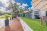 Waterfront backyard featuring a deck, synthetic turf lawn, concrete retaining wall, and sliding impact glass doors