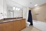 Bathroom featuring light wood cabinetry, stone-finish countertop with an integrated basin, large wall-mounted mirror, and a tub-shower combination wit