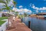 Waterfront property featuring a wooden deck, seawall, artificial turf area, and mature palm trees