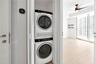 Stackable laundry unit featuring an Electrolux washer and dryer, digital wall-mounted thermostat, wood-finish flooring, ceiling fan with integrated li